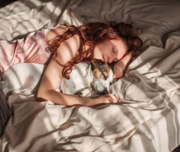 Frau liegt zusammen mit Hund schlafend im Bett.