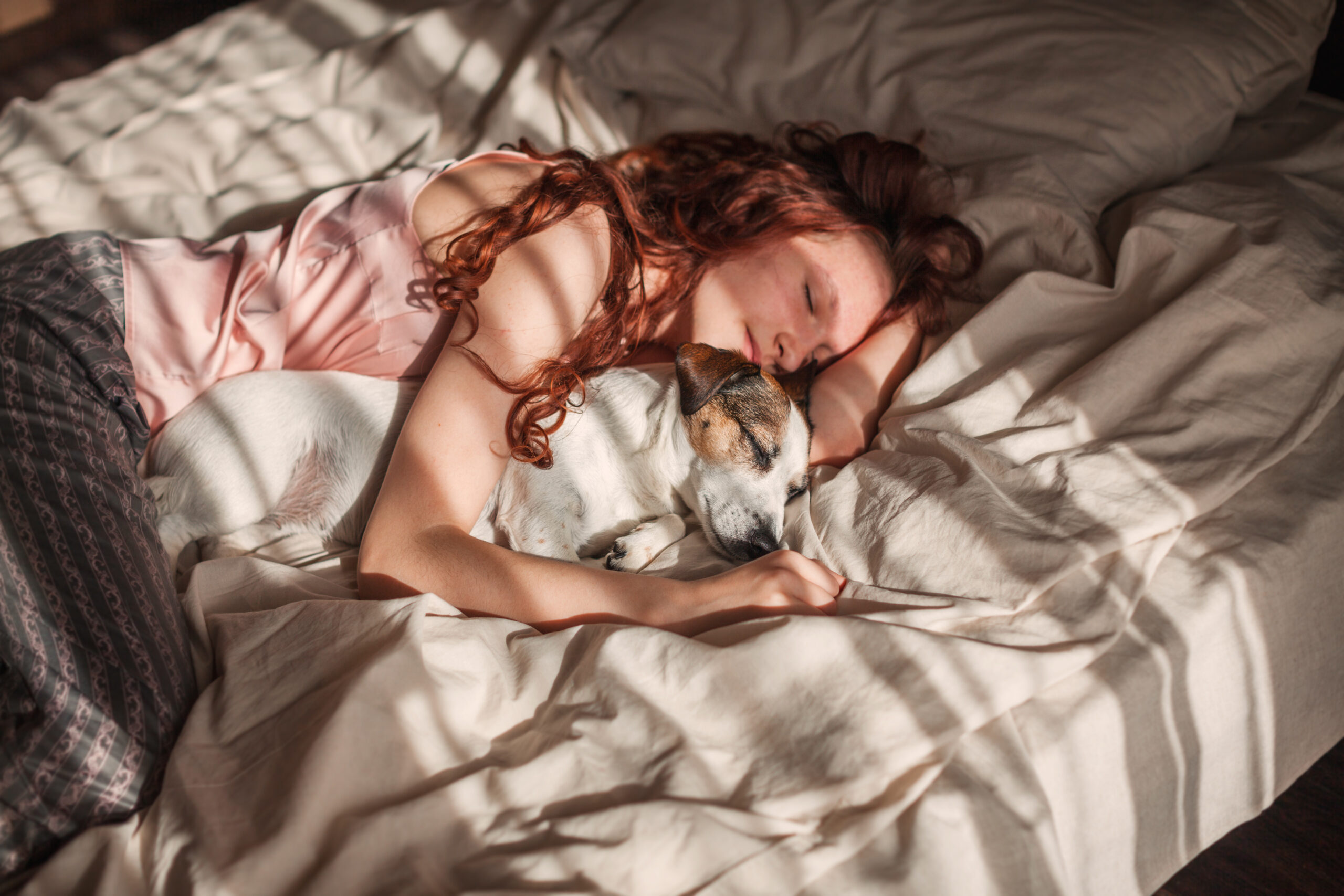 Frau liegt zusammen mit Hund schlafend im Bett.