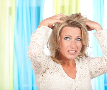 Frau zwischen 40-50 Jahren greift sich mit kritischem Blick in die Haare.