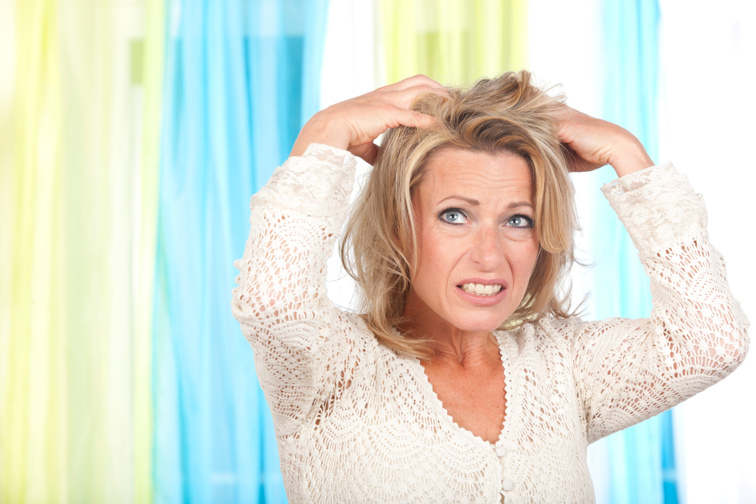 Frau zwischen 40-50 Jahren greift sich mit kritischem Blick in die Haare.