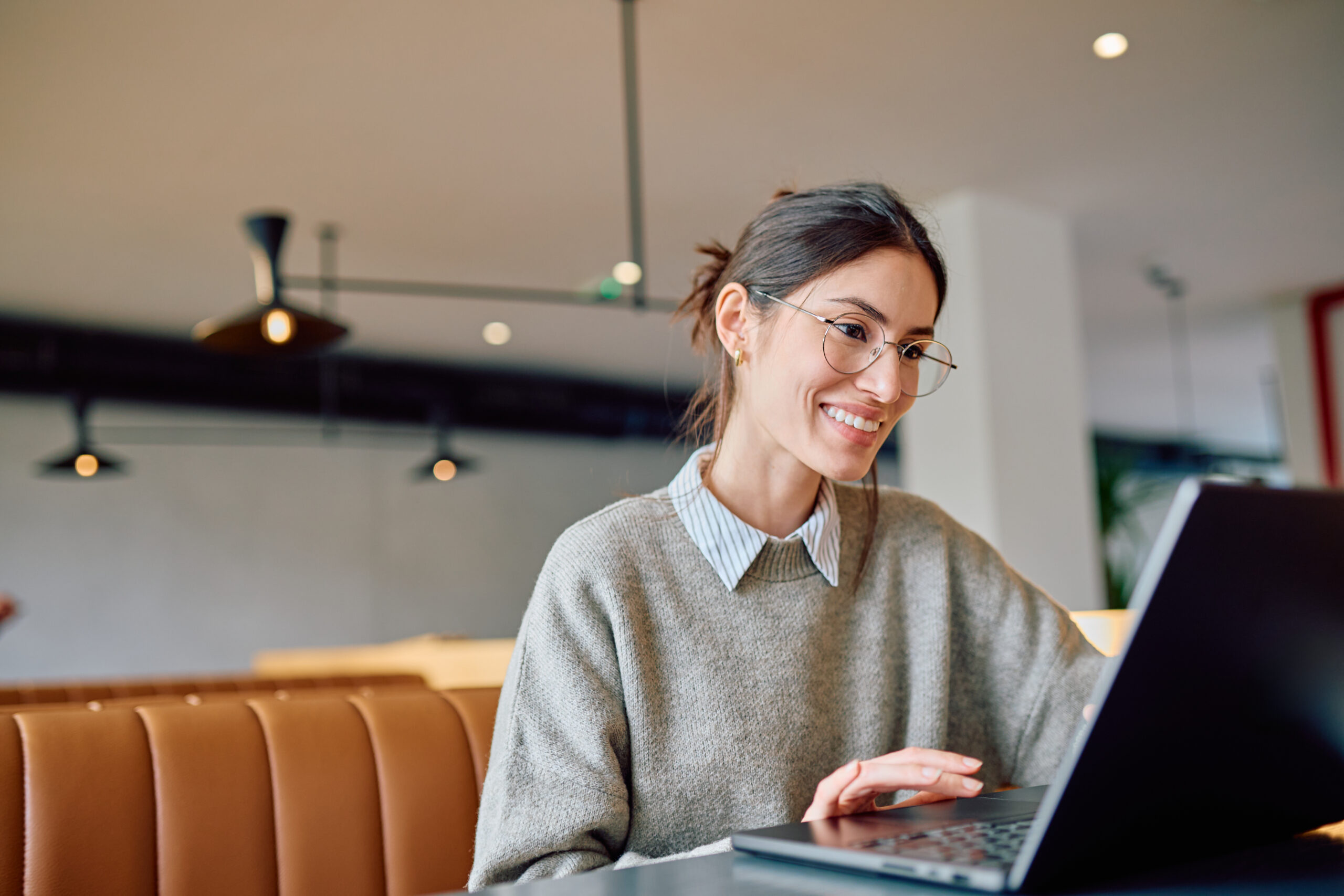 Frau mit Brille sitzt mit Laptop an einem Schreibtisch und lächelt.