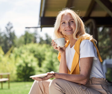 Frau im Alter von ca. 50 sitzt draußen und schaut zufrieden aus.