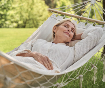Frau ligt draußen in einer Hängematte - symbolisch für Entspannung und Achtsamkeit.