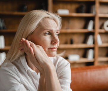 Blonde Frau in den Wechseljahren sitzt auf dem Sofa und sieht erschöpft aus.
