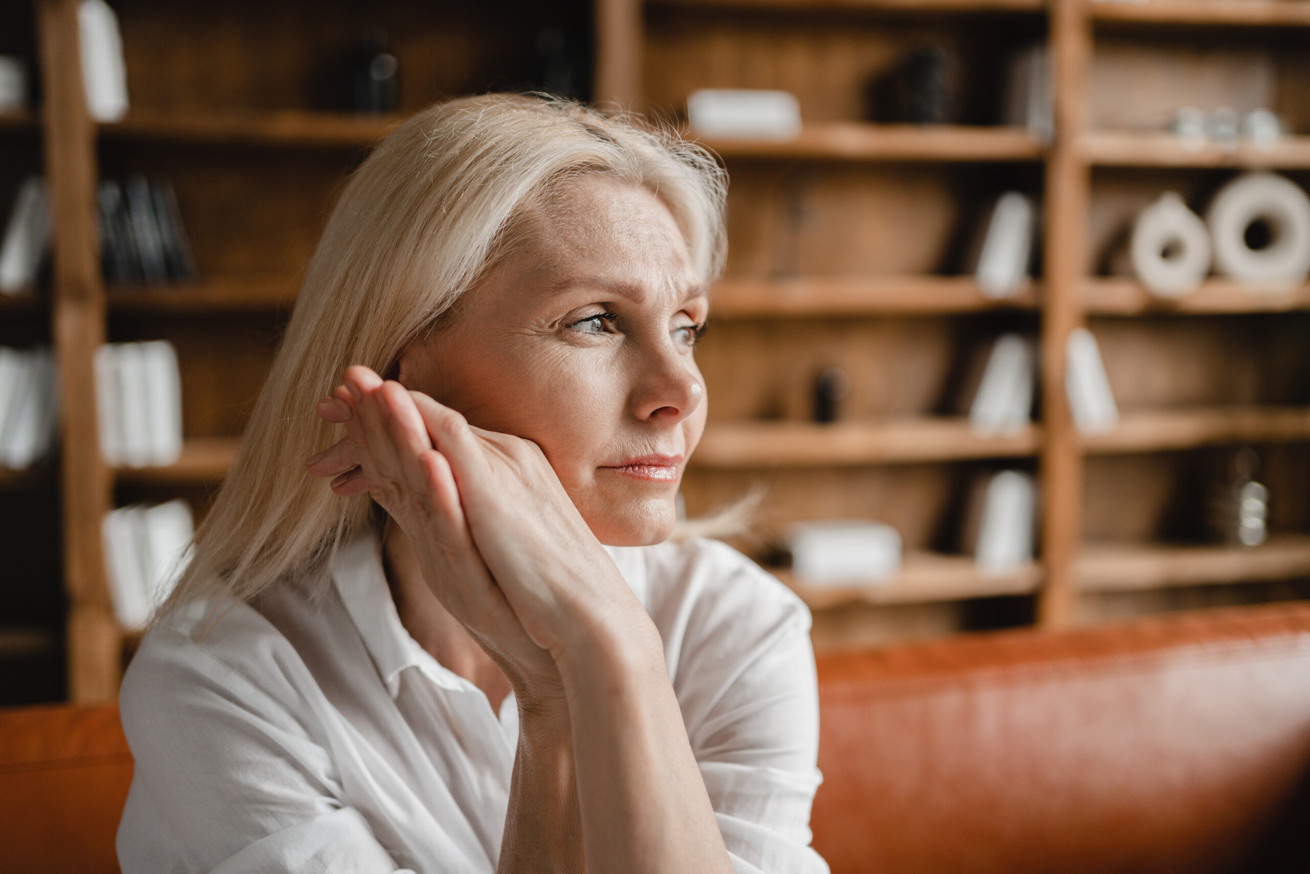 Blonde Frau in den Wechseljahren sitzt auf dem Sofa und sieht erschöpft aus.