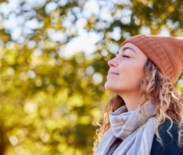 Frau ist in der Natur und hält das Gesicht mit geschlossenen Augen Richtung Sonne