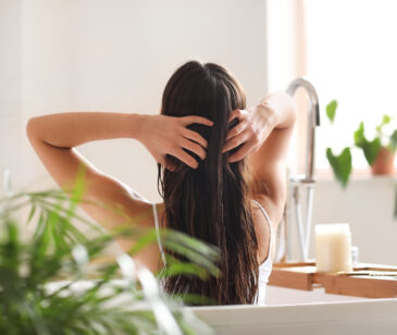 Frau mit langen Haaren sitzt in in einer Badewanne und fährt sich mit den Fingern durch das Haar.