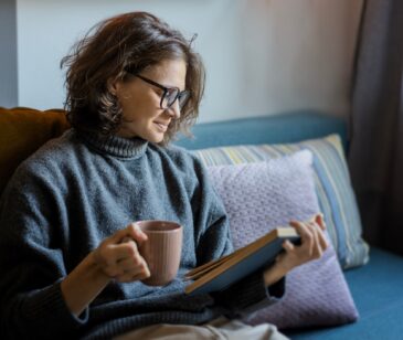 Eine Frau sitzt auf dem Sofa und liest ein Buch über die Menopause.