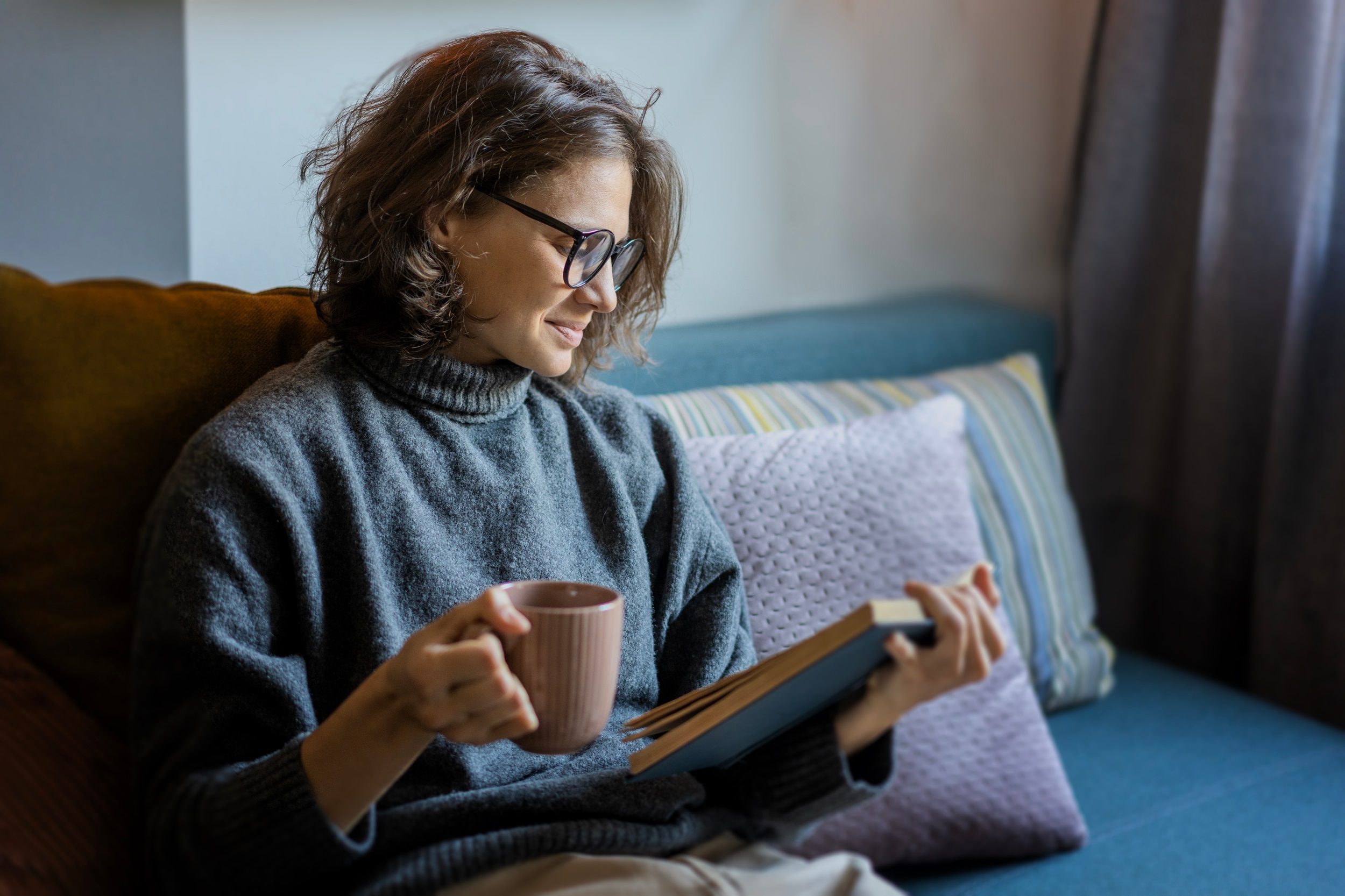 Eine Frau sitzt auf dem Sofa und liest ein Buch über die Menopause.