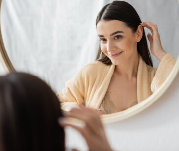 Junge Frau schaut selbstbewusst und glücklich in den Spiegel.