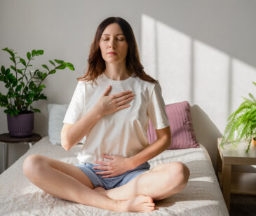 Frau sitzt auf dem Bett und macht eine Atemübung.