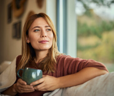 Frau sitzt entspannt mit einer Tasse und Decke auf dem Sofa